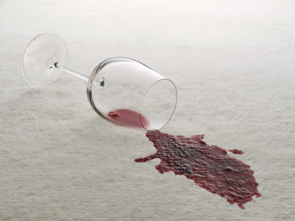 An overturned wine glass with red wine spilled on a white carpet, now a job for Sammamish Carpet Cleaning.