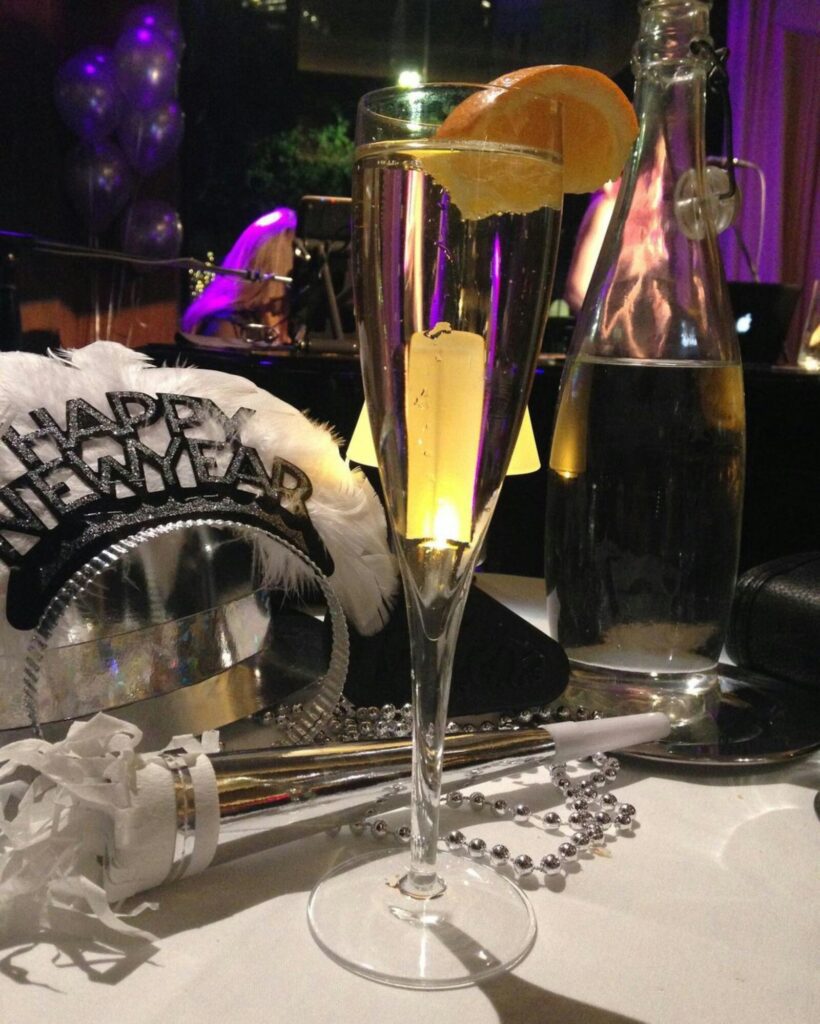 Celebratory New Year's setup with a champagne glass, party hat, noise maker, beads, and a water bottle on a table.